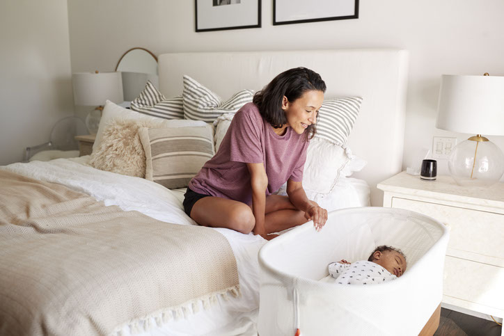 Mom sitting on bed looking down at baby in bassinet